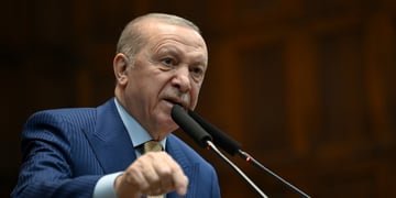 Recep Tayyip Erdogan in blue siot, baby blue shirt in front of two black vertical picrophones