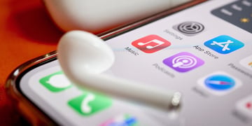 Airpod on top of iPhone screen displaying Apple Music app, Podcasts