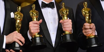 four golden oscars statues held in four mens hands in black suits