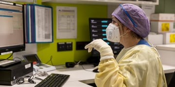 female nurse, blue har net, yellow scrub, computer monitor, white gloves, green wall