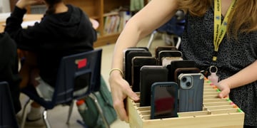 Teacher Heather Debby carries a box filled with students' cellphones in a classroom
