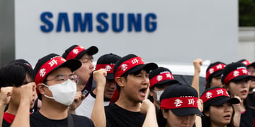 crowd of people with red bands around black hats chanting, samsung blue sign