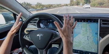 tesla black driving wheel, road ahead, two white hands not touching the wheel, map on screen