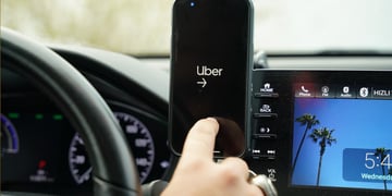 uber app open on black smartphone screen, car screen, blue sky and palm tree, driving wheel