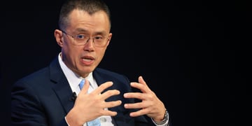 Changpeng Zhao, asian man, hands up to chest level, fingers apart, glasses, black suit, background