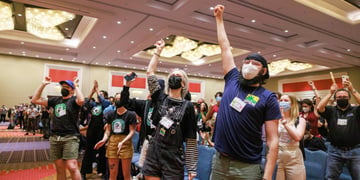 people with one hand up, white, black respirators, dark blue t-shirt, green shorts,  orange carpet 