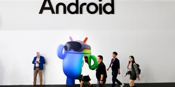 three asians walk pass blue android mascot, white wall, one man leaning to wall, Android black sign