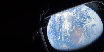 female astronaut looks from dark spacecraft cabin to blue earth in space