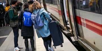woman runs to train, open doors, long light brown hair, sky blue coat, heavy luggage