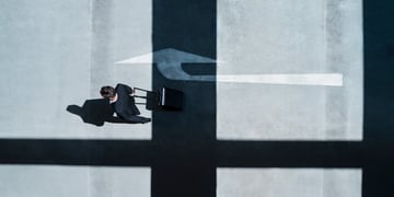 Businessman, black suit, suitcase arrow shadow on grey pavement