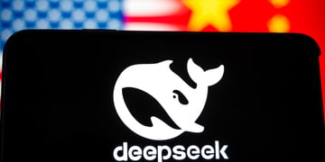 DeepSeek app logo with white whale on black phone screen, blurry  US and China flags in the back