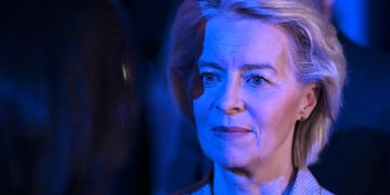 Ursula von der Leyen, blonde woman, semi-smile, white skin lit up in dark blue light 