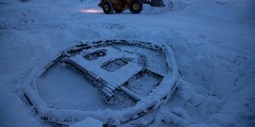 bitcoin logo sculpture made from scrap metal, frozen on snow, mining truck in the background
