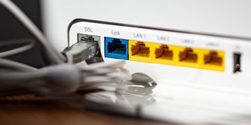 A grey LAN cable is plugged into the grey DSL slot of a white WLAN router, yellow, blue slots