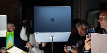 Dark grey MacBook Neo laptop computer, Asian people around it in the dark taking pictures