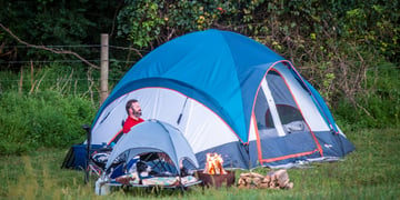blur and white tent, bearded man in red shirt, mini blue tent with dog resting, green grass