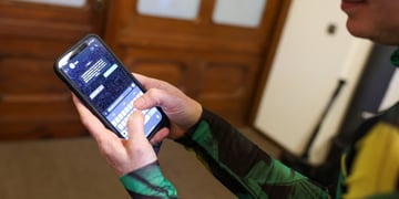 woman in green, black right top holds smartphone, shows screen with text messages, brown door