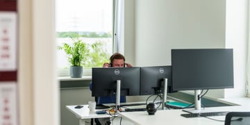office worker with headset, hands up, crear window, green tree, three dell monitors, white desks 