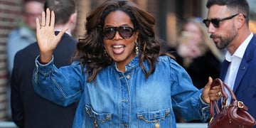 Oprah Winfrey waves right hand, jeans jacket, brown purse, brown sunglasses, white man, 