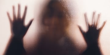 A shadow of a rape victim behind glass.