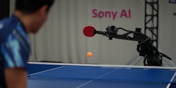 black robot hand, red racket, blue table tennis table, human player, black hair, blue shirt