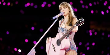 Taylor Swift, pink-violet sparkly bodysuit, pink guitar, white microphone, dark stadium crowd