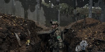 ukrainian soldier in muddy trench, uniform, muddy face, ruins around, gun on shoulder, helmet