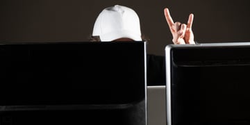 white baseball hat on head behind two black screens, rock and roll fingers in the air