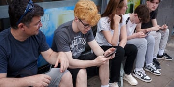 yellow curly hair, young white teen, grey tshirt, smartphone, three other people, glasses