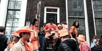 people dressed in orange, amsterdam streets, man on phone, sits on stairs, big windows
