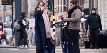 male and female tourists, darker skin, black smartphone, two dark blue luggages, pedestrian