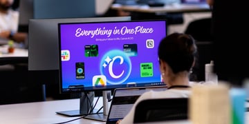 Employee at white desk, black screen frame, violet canva logo on screen, office, dark short hair