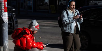 woman, red puffy jacket, woman i nblack pants, light blue jeans jacket, two smartphones, scroll