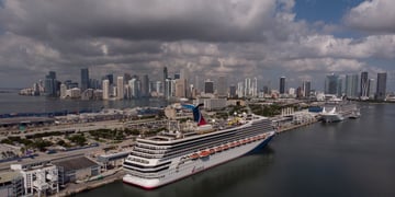 huge white Carnival cruise ship Sunrise docked in post, cloudy blue sky, miami shore, tall homes
