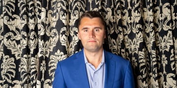 Charlie Kirk standing in front of a decorative curtain.