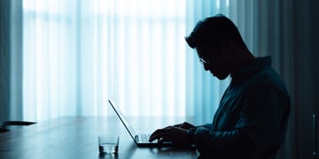 man profile from left, blue lighting, desk, light curtains, laptop, 