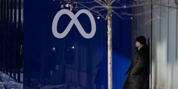 dark grey meta logo on dark blue wall, winter, woman in long black winter coat, blonde, 