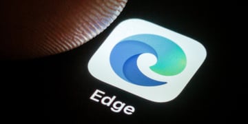 microsoft edge blue-greenish icon in white background on black screen, finger tip