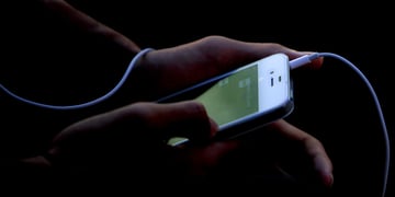 white iphone, green screen, plugged in headphone white wire, hands taping screen, darkness