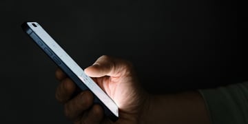 white phone screen held inright hand, shown from profile, dark room