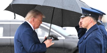 donald trump, dark blue jacket, looks at black smartphone, big black umbrella, rain, grey sky