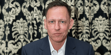 Peter Thiel, dark suit, white collar shirt, no tie, dark hair, light eyebrows, smirk