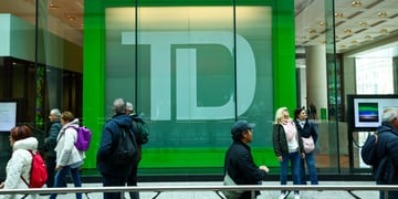 TD bank logo in green behind glass wall, about ten pedestrians walking in warm clothes