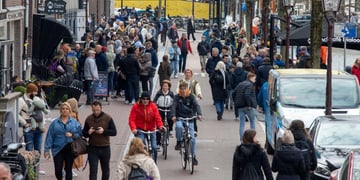 busy street filled with white pedestrians, cyclists, red jacket, water canal, blue jeans jacket