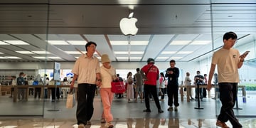 middle aged white asian couple exit apple store, logo, pink pants, black hair, glass wall, white tshirt