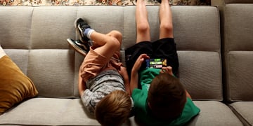 two white boys, green t-shirt- black shorts, grey t-shirt, light grey sofa, roblox on iphone screen