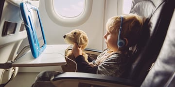 blonde boy, on flight, white plane salon, light brown teddy bear, baby blue tablet with wire