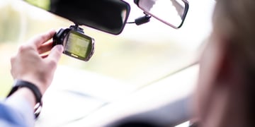 black dash camera attached to rear view window, white male hand, baby blue sleeve