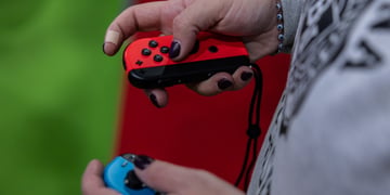 nintendo joy con held in white female hands, grey jumper, grass green background
