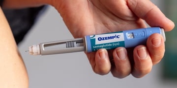 white person belly, white hand, baby blue ozempic pen, grey wall